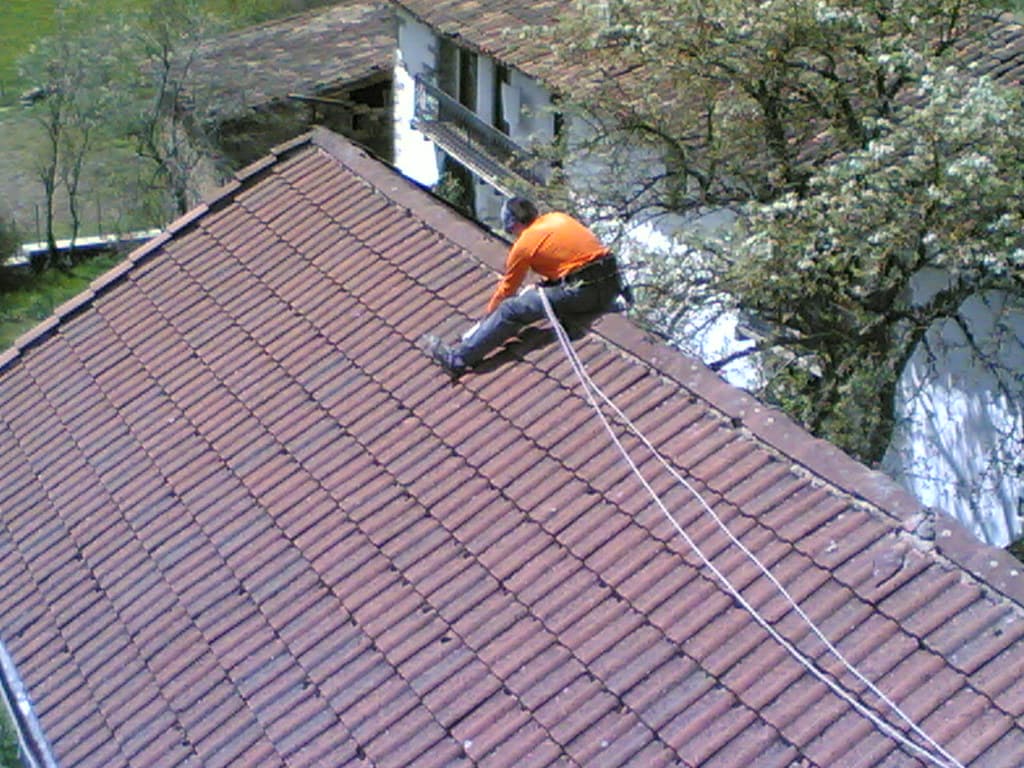 A roofer working along the ridge of a terracotta tile roof