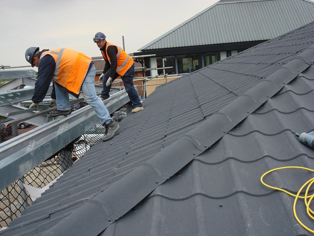 Two roofers in high visibility safety vests working on a grey concrete tile roof