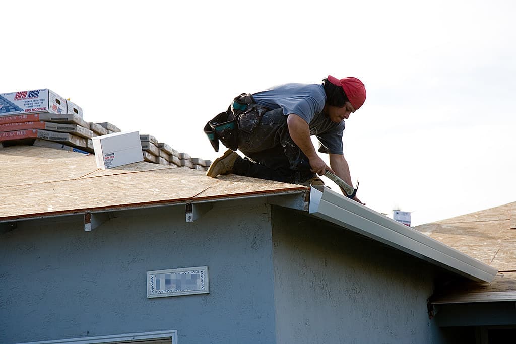 A roofer fitting a new metal gutter along a roofline