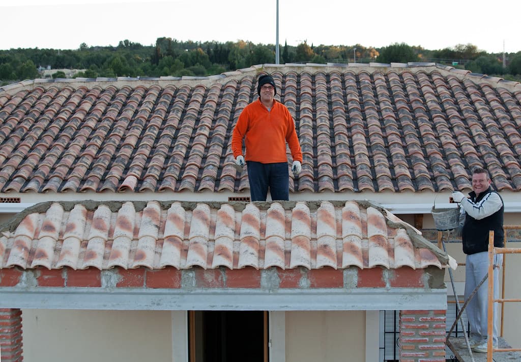 Two roofers repointing and resealing ridge capping on a terracotta tile roof